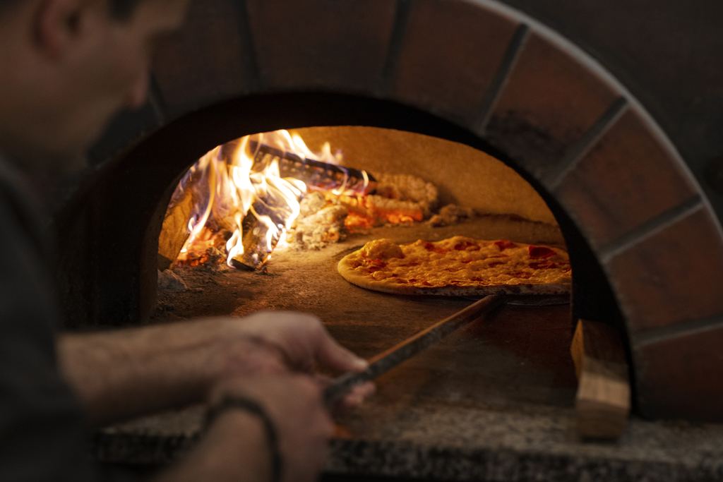 Pizzaiolo baking a pizza inside a glowing wood-fired oven