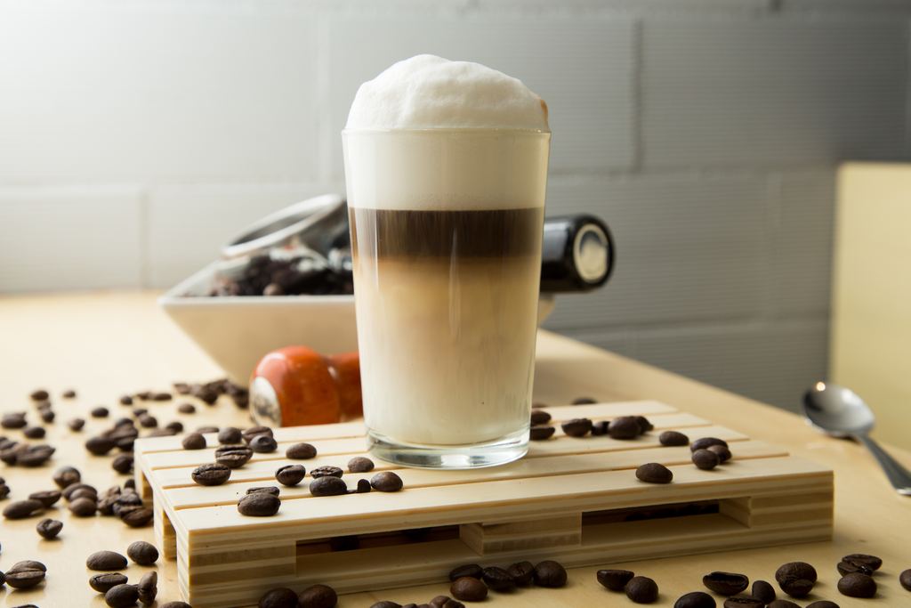 Barista pouring milk to finish a flat white coffee in a cafe