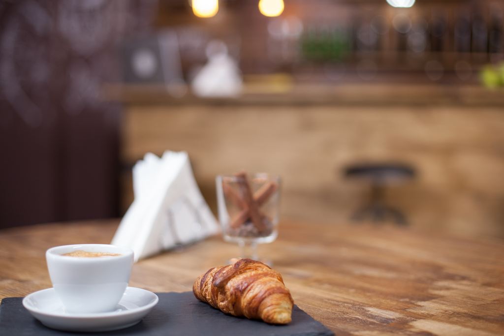 A croissant and a cup of coffee served on a cafe table in warm morning light