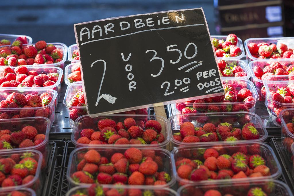 Punnets of strawberries on a market stall behind a small chalkboard with the price handwritten on it