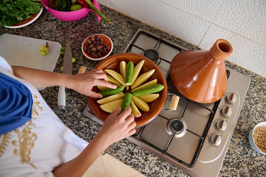 Hands arranging vegetables in a clay pot while cooking a Moroccan tagine