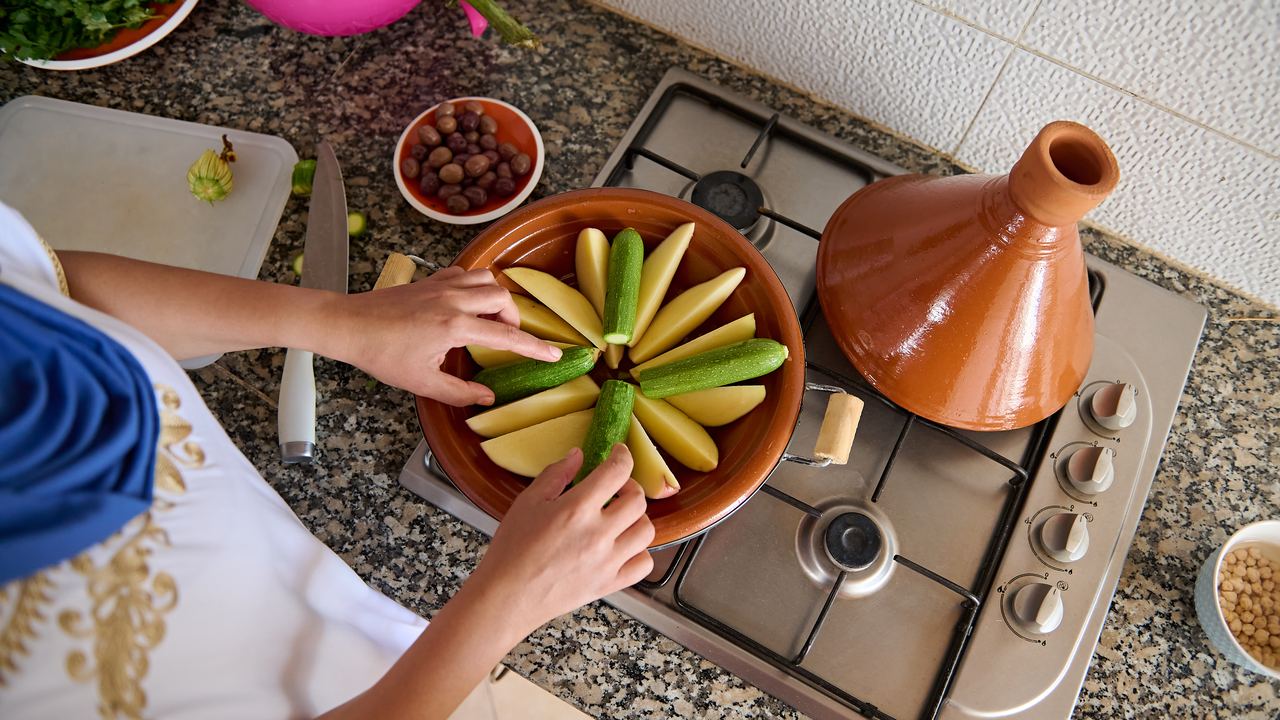 Hands arranging vegetables in a clay pot while cooking a Moroccan tagine