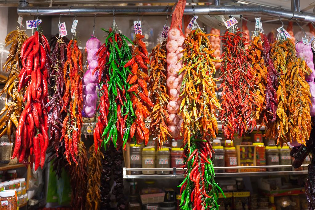 Strings of dried red chilli peppers and garlic hanging at a market stall