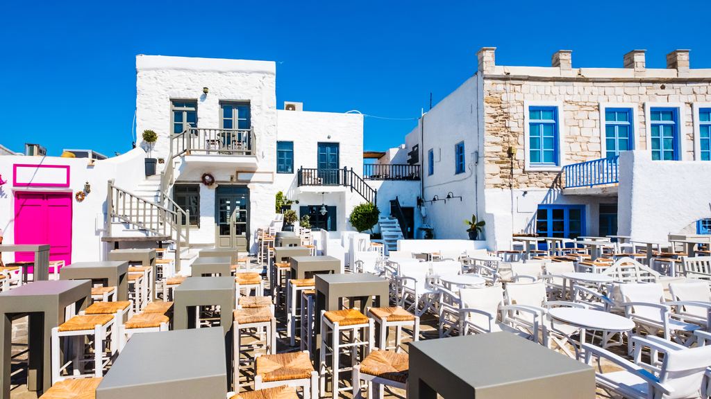 A Greek taverna with brightly coloured tables and chairs set out along the waterfront
