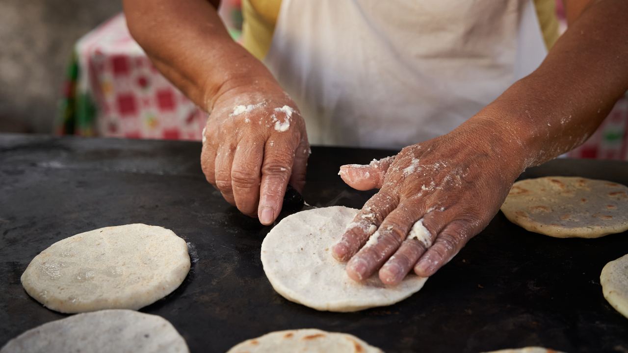 Woman flipping a handmade corn tortilla on a hot griddle