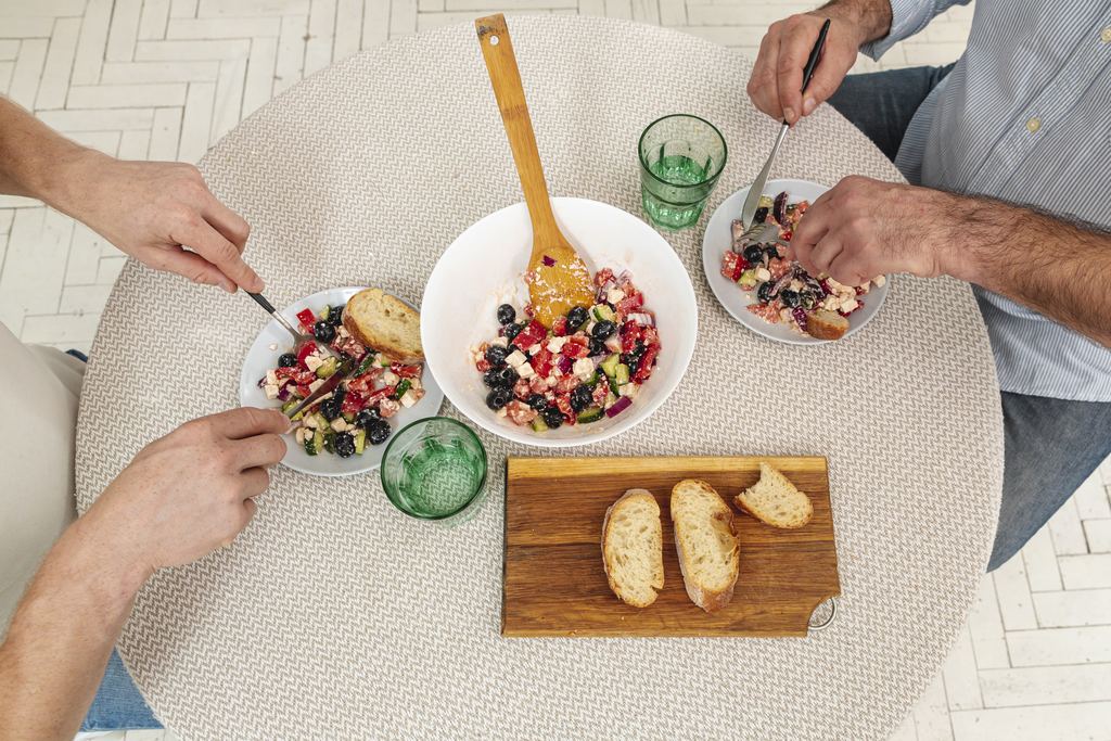 Overhead view of three people around a small table passing plates and serving each other from a shared bowl of food.