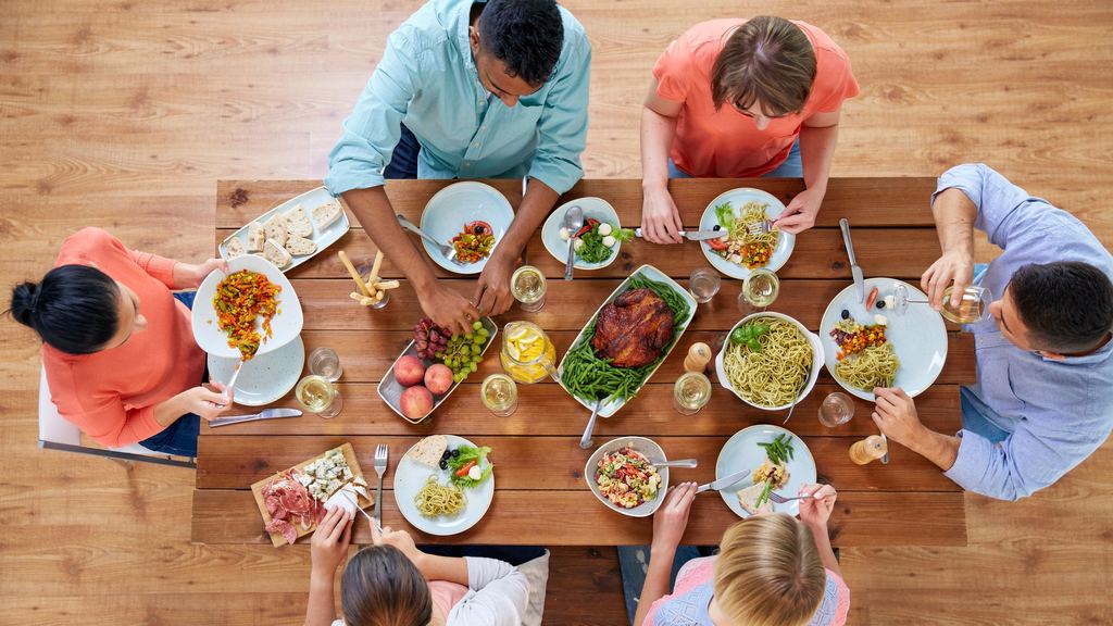 Overhead view of a long wooden table where a group eats together, plates and glasses spread across it