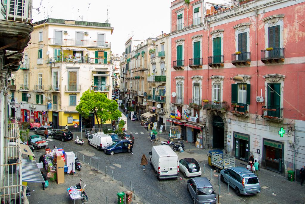 Busy Naples street in the morning, scooters and people passing old colourful buildings