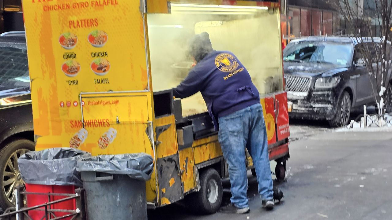 Yellow halal street food cart with vendor cooking on a New York City sidewalk