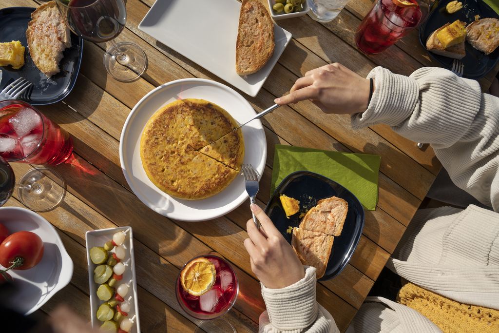 Hands reaching for slices of Spanish potato tortilla served on a bar counter
