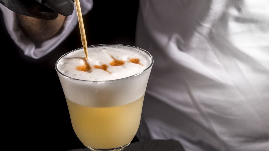 A bartender finishing a pisco sour with drops of angostura bitters