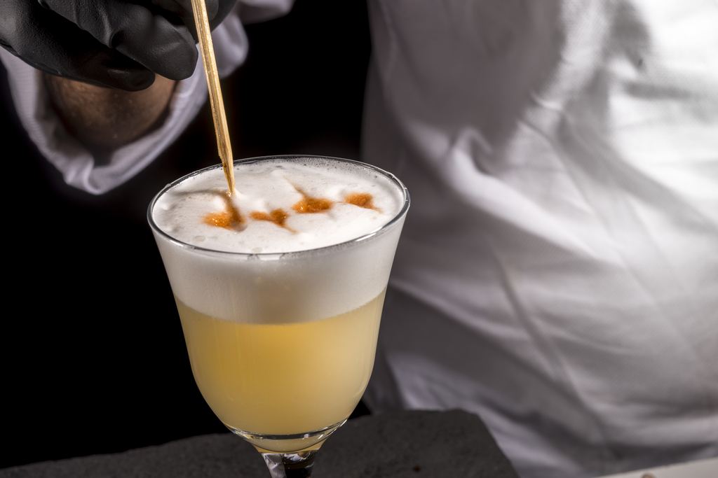 Bartender finishing a pisco sour with drops of angostura bitters