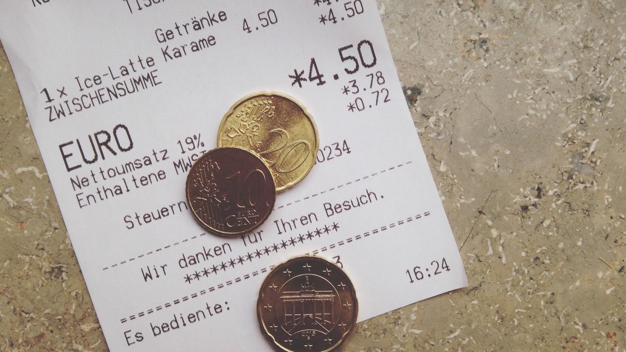 A printed restaurant receipt lying on a table with euro coins resting on top of it, seen from above