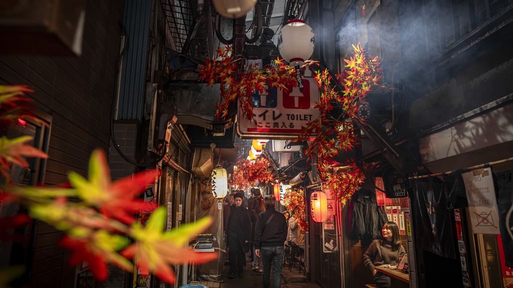 Visitors walking slowly through a narrow alley of small bars and lit signs at night