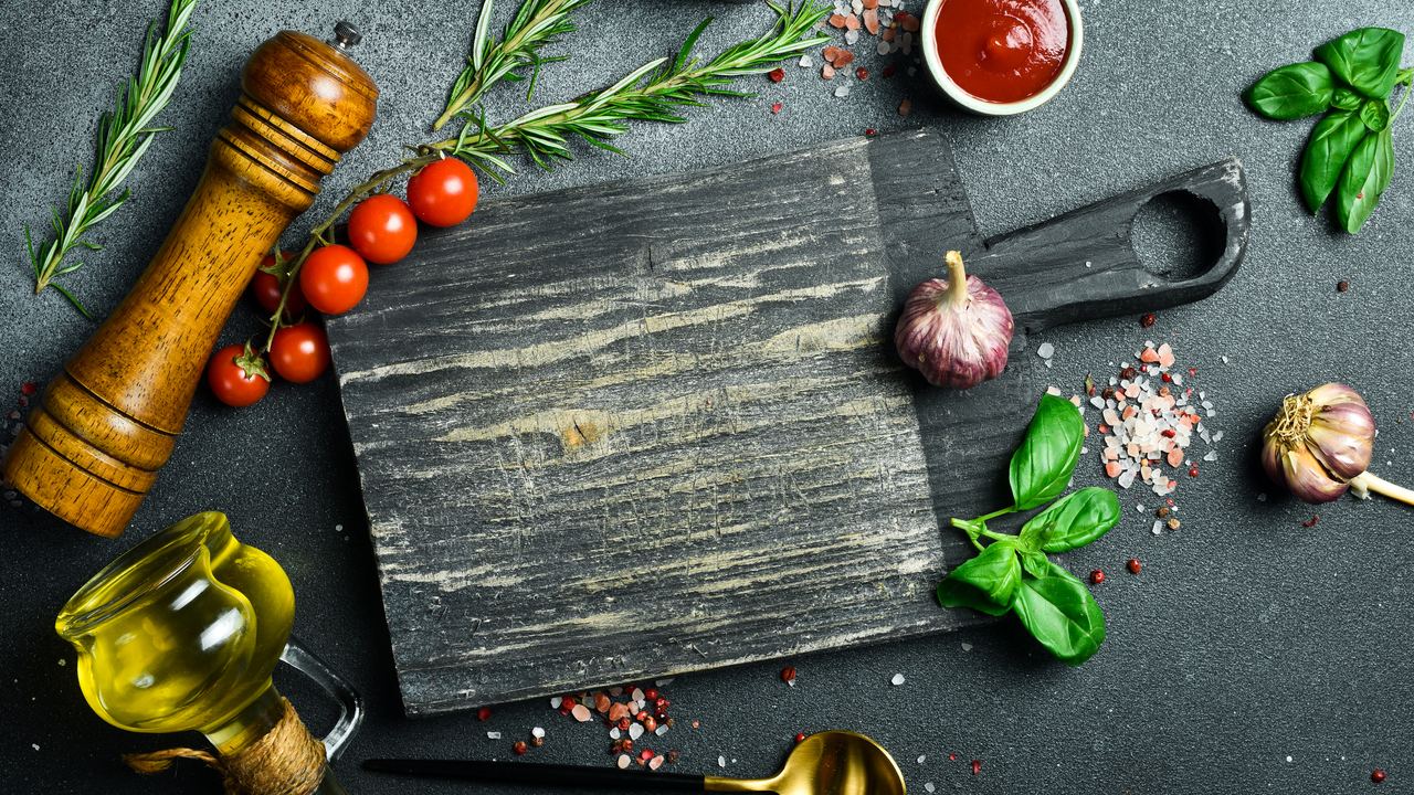 Wooden board with herbs and spices arranged on a dark stone surface