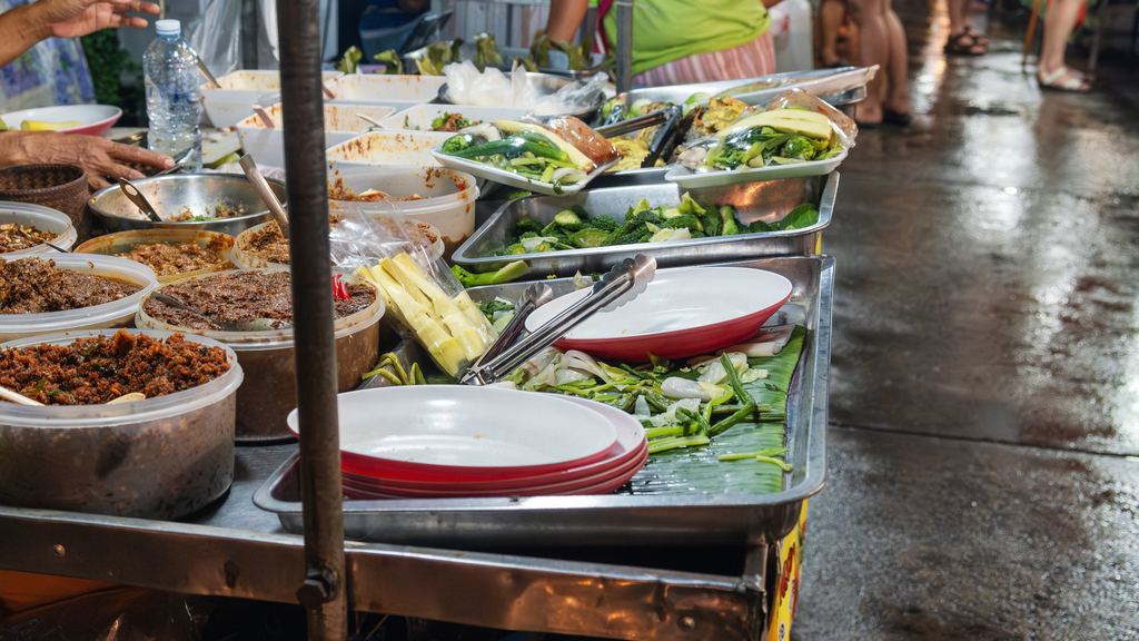 A Thai street food vendor stall with prepared dishes and vegetables at a night market