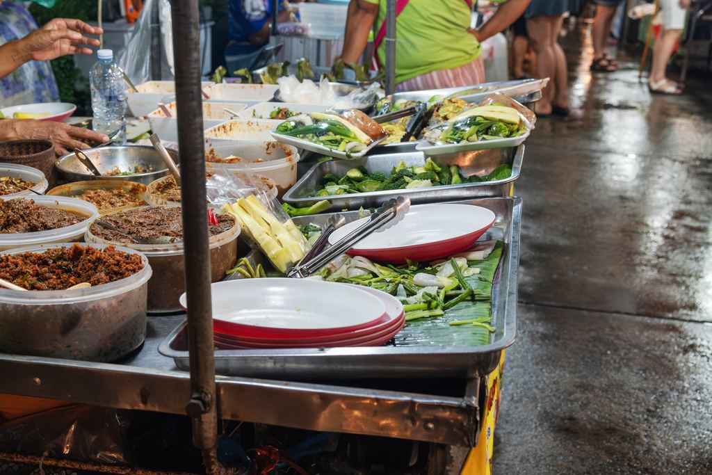 Thai street food vendor stall with prepared dishes and vegetables at a night market