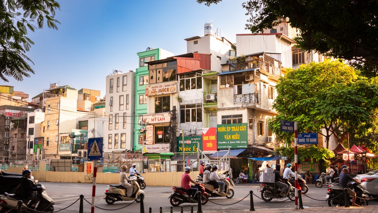 Busy Vietnamese street with people riding scooters past shopfronts in Hanoi