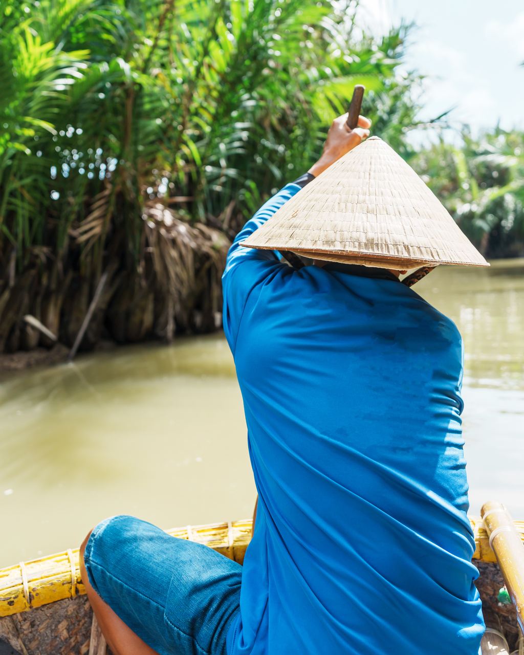 Man rowing a round bamboo basket boat through the water coconut palms near Hoi An