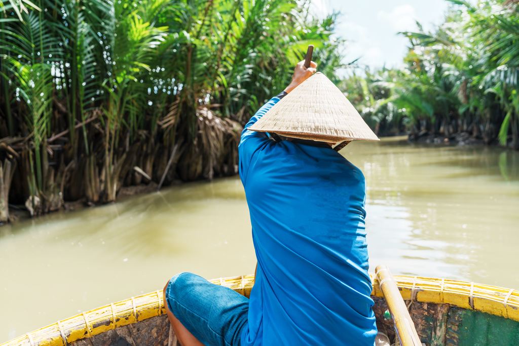 Man rowing a round bamboo basket boat through the water coconut palms near Hoi An