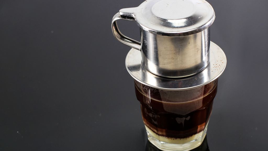 Glasses of Vietnamese coffee with condensed milk beside a traditional phin drip filter