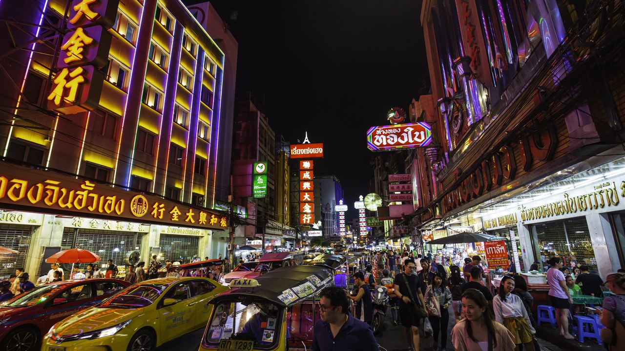 Busy Yaowarat Road in Bangkok Chinatown at dusk, lined with lit shop signs
